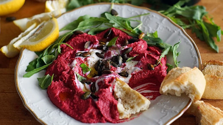 Červený hummus s jogurtem a okurečkou na talíři