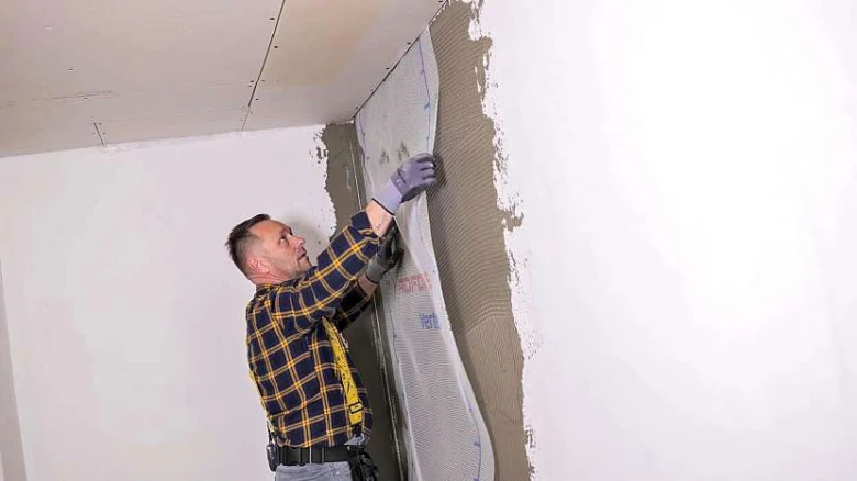 Muž nanáší lepidlo na zeď při instalaci perlinky