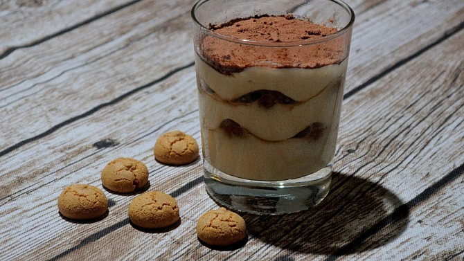 Tiramisu ve sklenici s kakaovým práškem a sušenkami