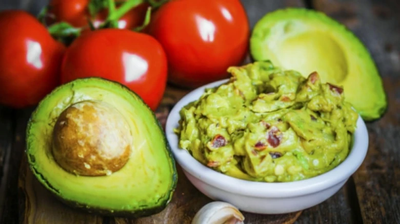 Avokádo, guacamole a rajčata na dřevěném podkladu