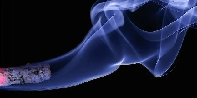 Zapálený cigaretový doutník s modrým kouřem na černém pozadí.