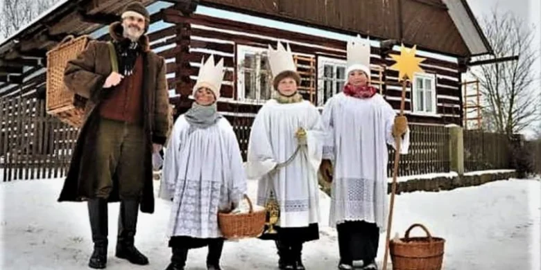 Tři králové v tradičních kostýmech na sněhu před dřevěnou chalupou
