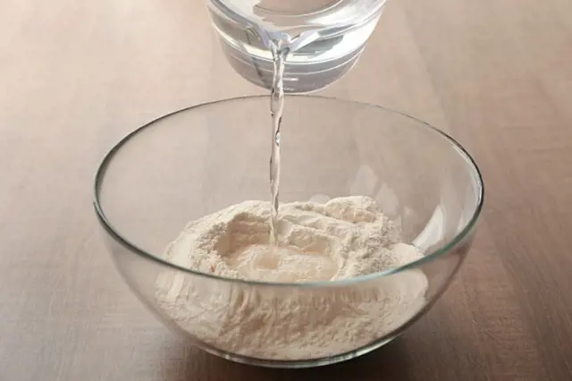 Voda se nalévá do misky s moukou pro přípravu plackového těsta