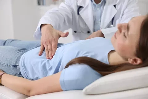Lékař vyšetřuje břicho ženy ležící na lůžku