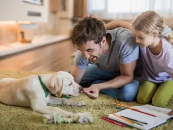 Otec s dcerou hraje s štěnětem doma na podlaze
