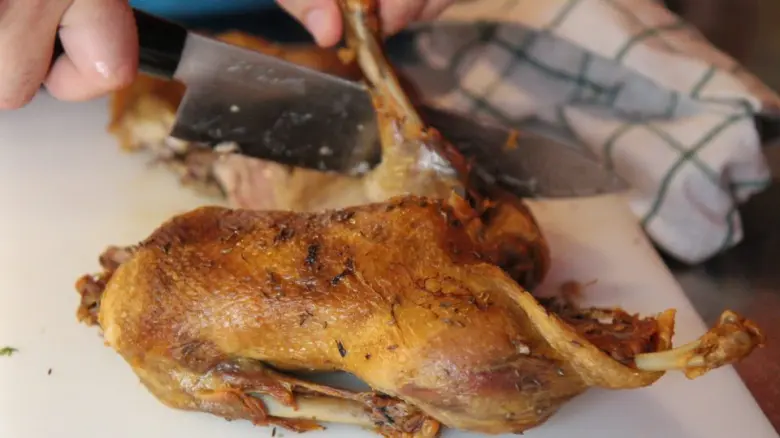 Osoba řeže pečenou kachnu na bílém desce