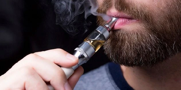 Muž s vousy kouří elektronickou cigaretu.