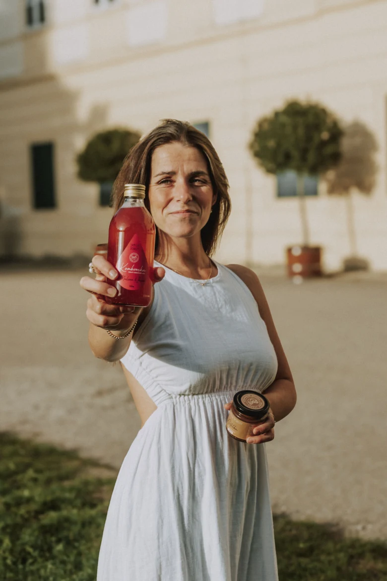 Žena drží láhev s kombuchou venku před budovou