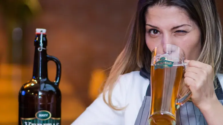 Žena pije světlé pivo z velkého skleněného poháru.