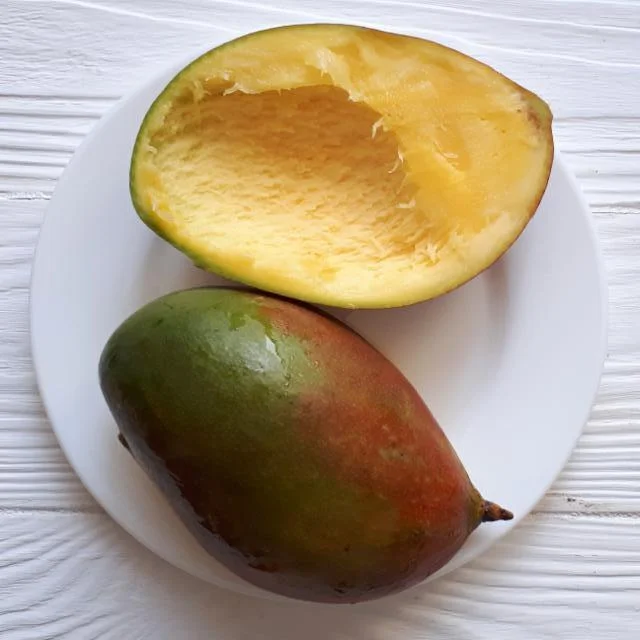 Polovička manga s dužinou a celý neoloupaný mango na bílém talíři.