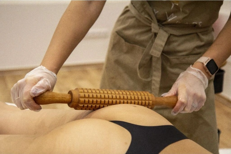 Terapeutka používá dřevěný válec pro masáž nohy.