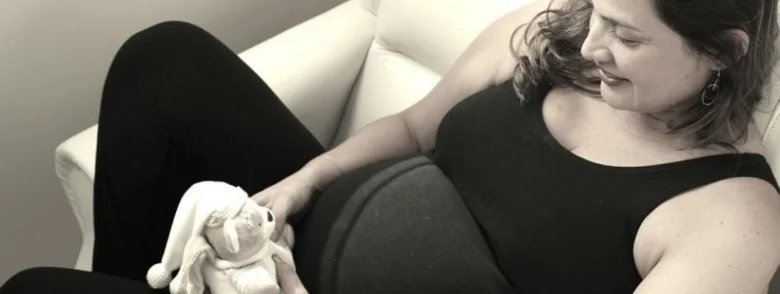 Těhotná žena sedí na gauči s hračkou v klidu.