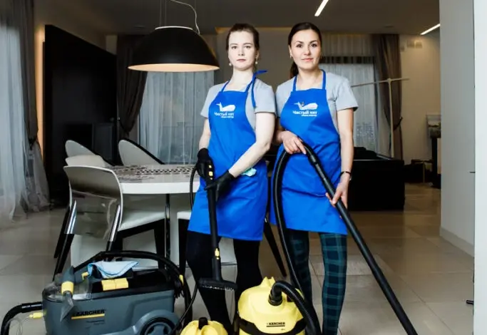 Dvě ženy s vysavači v modrých představeních udržují domácnost.