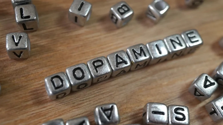 Stříbrné kostky s písmeny tvořící slovo dopamin na dřevě.