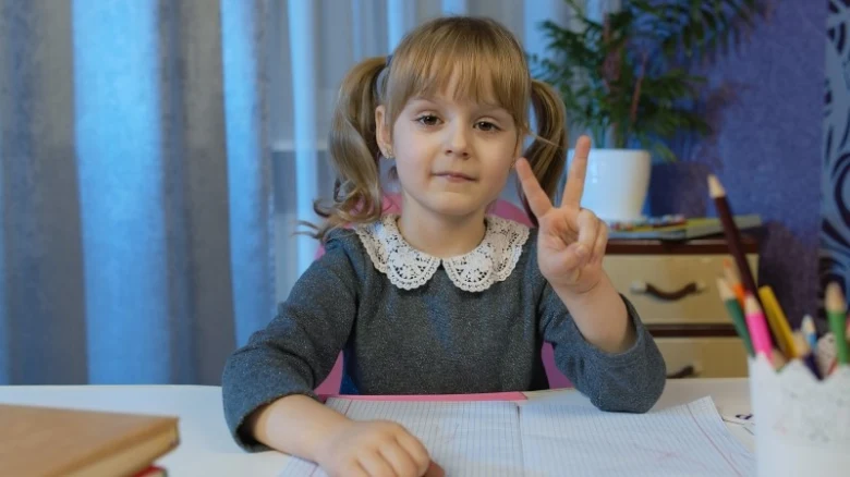 Malá dívka sedí u stolu a dělá pět prstů.
