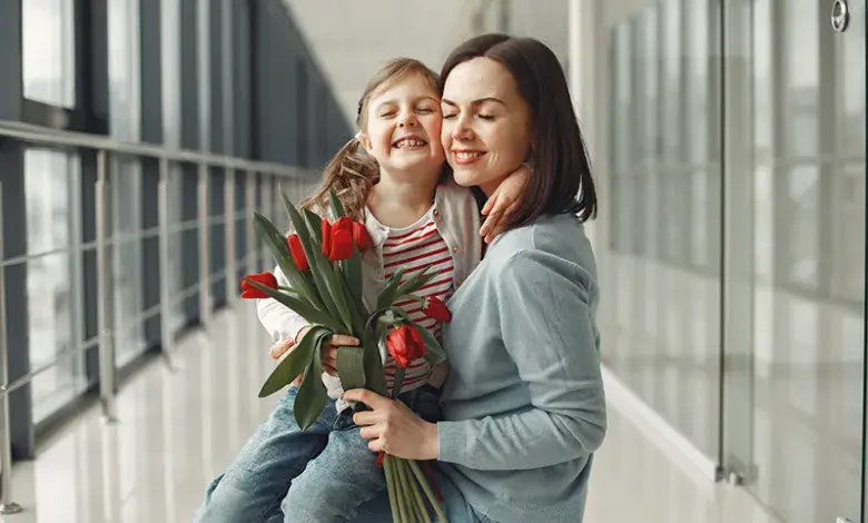 Matka s dcerou drží svazek červených tulipánů v chodbě.