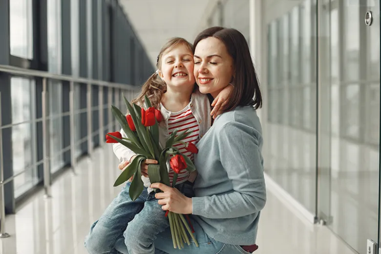 Matka s dcerou drží svazek červených tulipánů v chodbě.