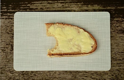 Kousek toastu s naneseným máslem na bílém prkně.