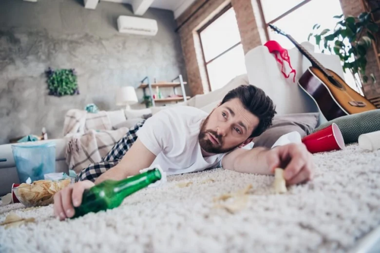 Muž leží na zemi po pití alkoholu s lahví piva a chipsy.