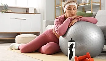 Žena v růžovém sportovním oblečení odpočívá vedle fitbalu.