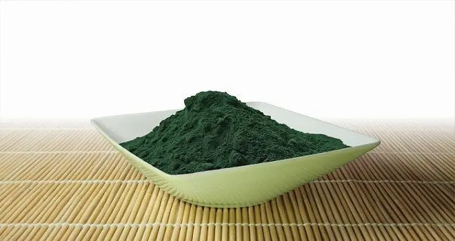 Mísa s tmavě zeleným práškem z řasy spiruliny na bambusové podložce.