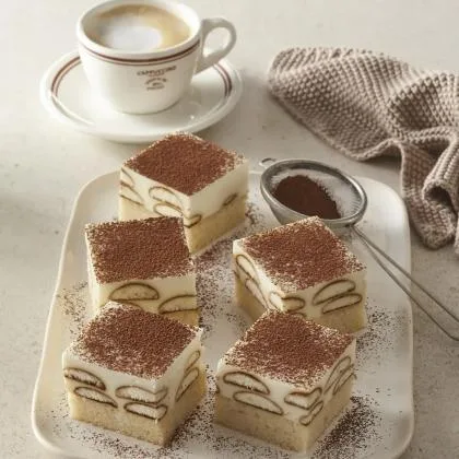 Tiramisu se mascarpone na talíři vedle kávy.